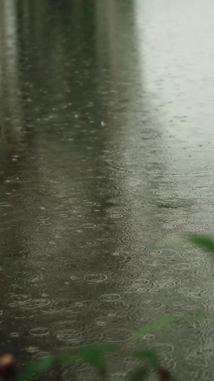 Experience heavy rain pouring over Bali's streets in this high-quality vertical video. Capturing serene raindrop patterns, a tranquil atmosphere prevails, making it ideal for mobile stories