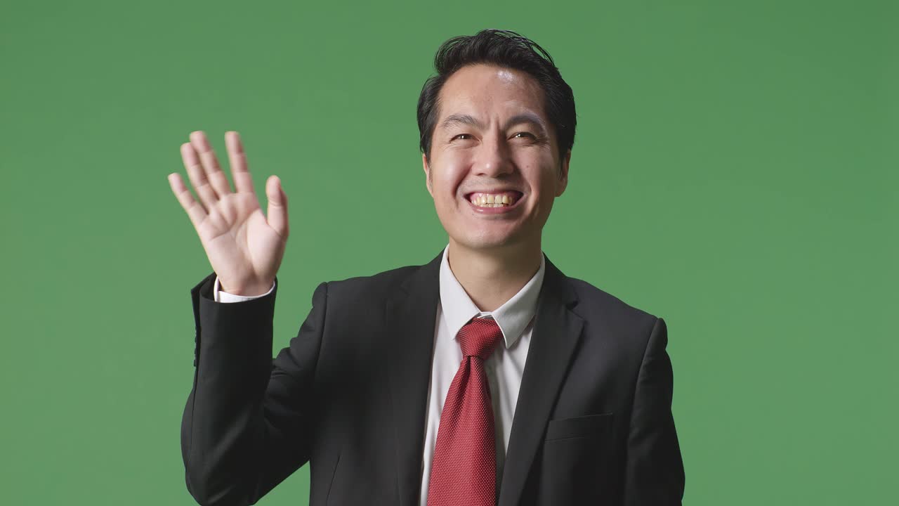 스튜디오에서 녹색 스크린에 서서 손을 흔들고 미소 짓는 아시아 사업가