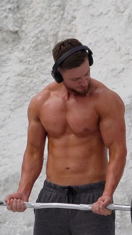training in the open air. athletic man doing exercise wearing wireless headphones vertical video