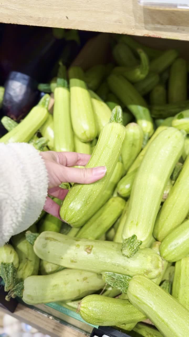 Hand picking zucchini from grocery display