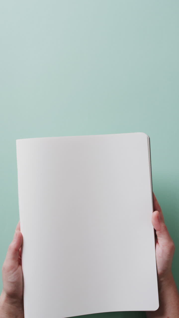 Vertical video of hand holding book with copy space on green background in slow motion