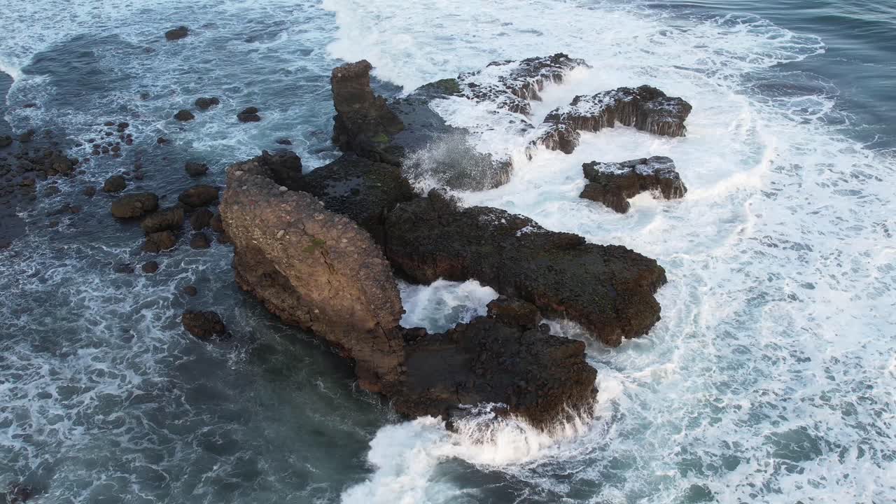 toma aérea estática de olas rompiendo en rocas en un océano azul