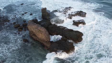 toma aérea estática de olas rompiendo en rocas en un océano azul