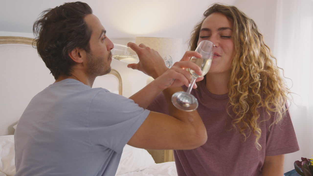 pareja enamorada con pijama en la cama en casa celebrando cumpleaños o aniversario con champán