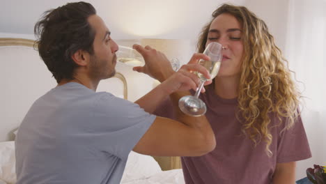 Loving-Couple-Wearing-Pyjamas-In-Bed-At-Home-Celebrating-Birthday-Or-Anniversary-With-Champagne