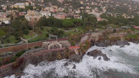 coastal genoa with waves crashing against rocks, rail tracks parallel to shoreline, aerial view