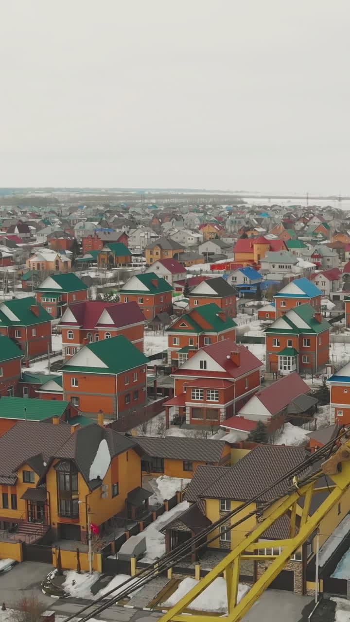 large cottage complex with green blue red rooftops and snowy park with little church and crane on foreground aerial view