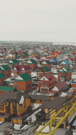 large cottage complex with green blue red rooftops and snowy park with little church and crane on foreground aerial view