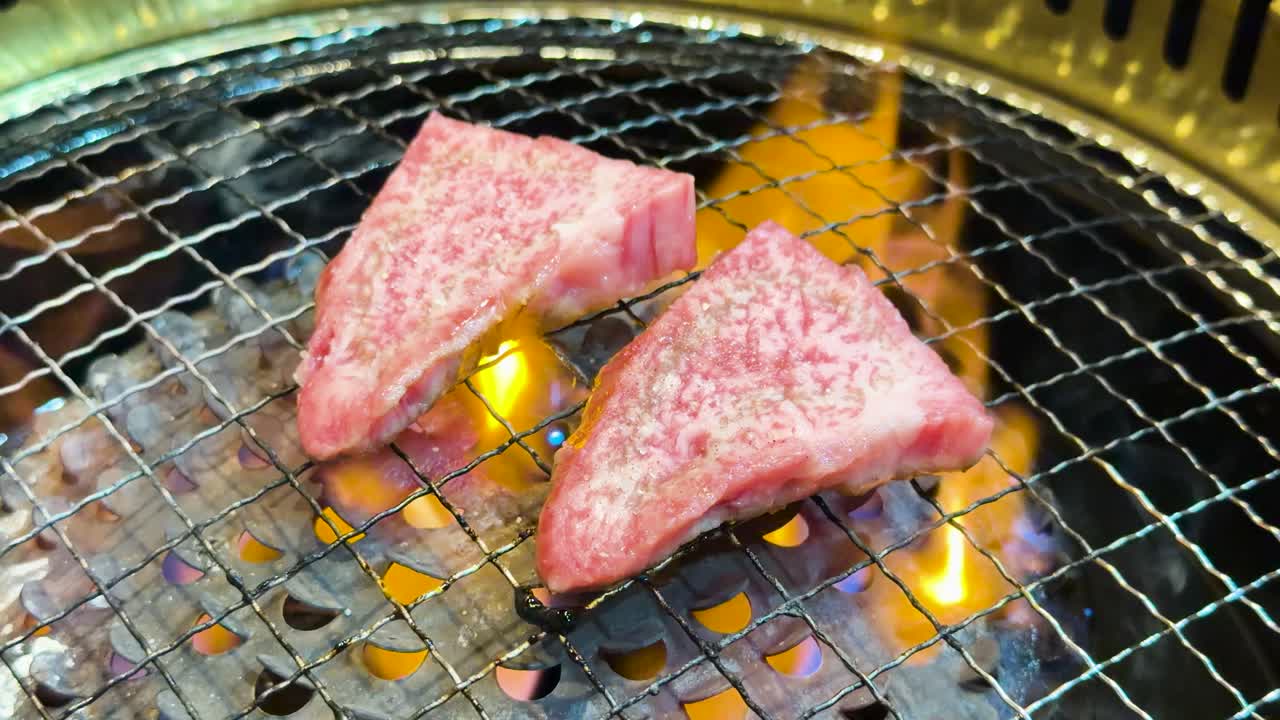 Nærbilde av marmorerte biffsteker som grilles på en rist med flimrende oransje flammer