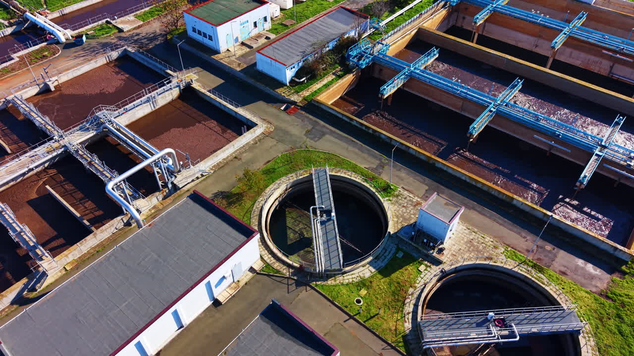 High angle drone shot of sewage treatment facility with rectangular aeration basins, blue metal walkways, and circular clarifier in the foreground
