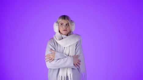 Blonde-Frau-Friert-Und-Reibt-Sich-Die-Hände-An-Den-Ärmeln-Ihres-Pullovers,-Gekleidet-In-Winterkleidung,-Studioaufnahme-Mit-Violettem-Hintergrund