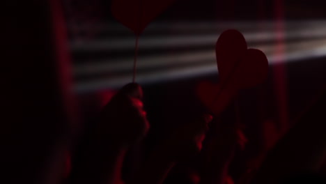 hands holding red heart-shaped signs at a vibrant concert with dramatic lighting effects