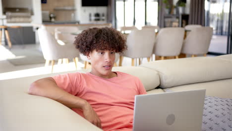 Un-Joven-Birracial-Está-Trabajando-En-Una-Computadora-Portátil-En-El-Sofá-De-Casa