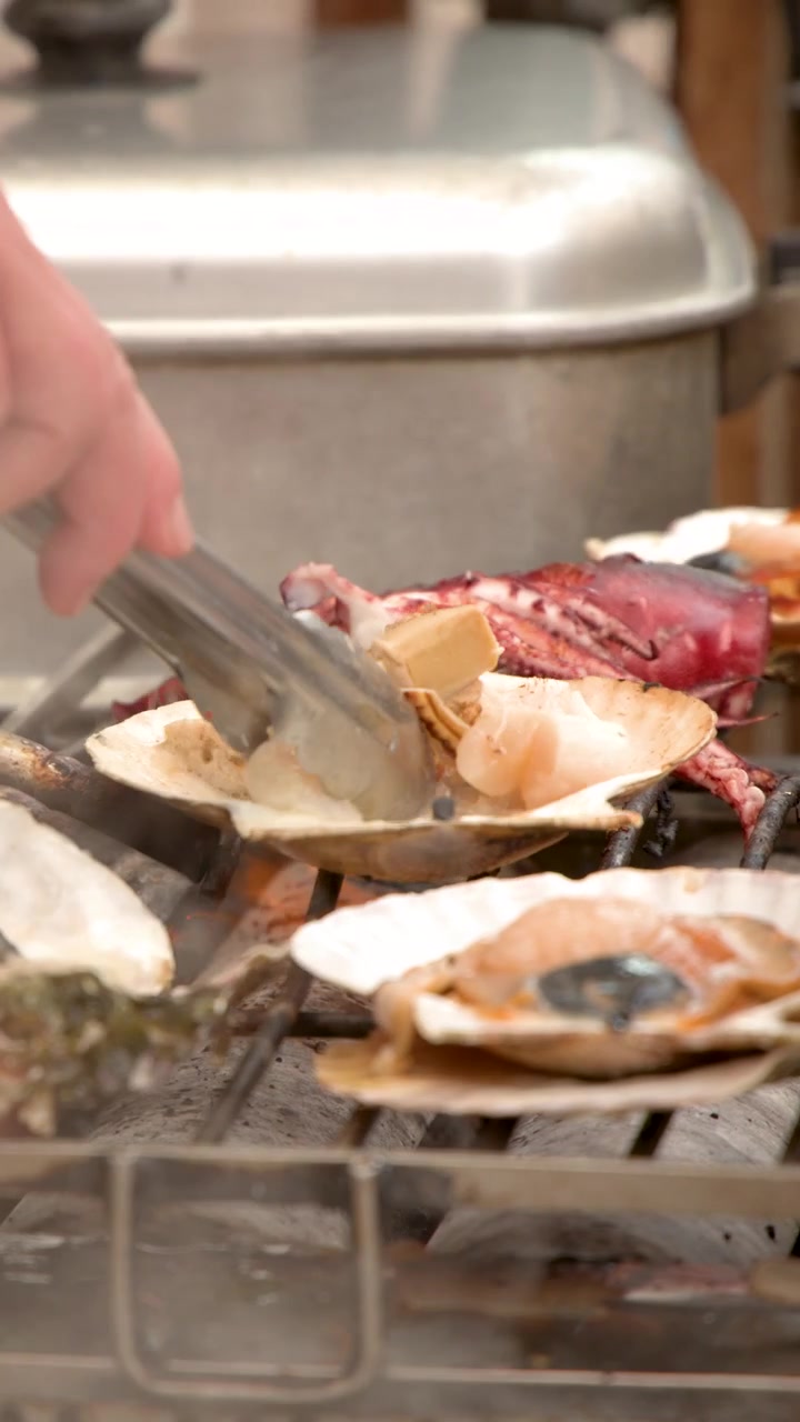 Close-up of a vendor using tongs to grill fresh scallops and seafood at a market