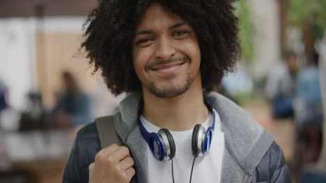 Retrato-De-Un-Joven-Estudiante-De-Raza-Mixta-Confiado-Sonriendo-Feliz-Mirando-La-Cámara-Viajando-En-La-Ciudad-Disfrutando-Del-Estilo-De-Vida-Urbano-Peinado-Afro-Fresco