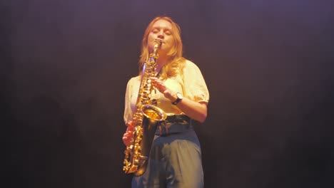 mujer joven tocando música en saxofón bajo las luces del escenario.