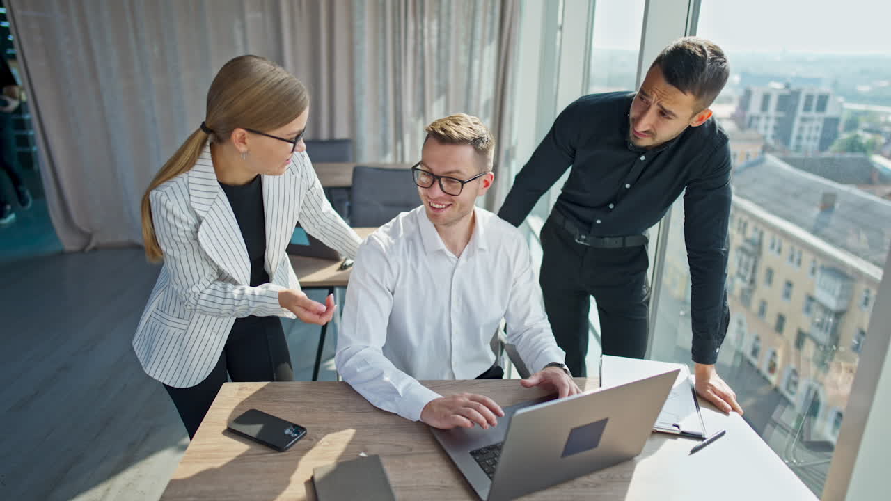 People cooperating at their work in office. Young teammates discussing something on laptop and laughing. Light office indoor backdrop.