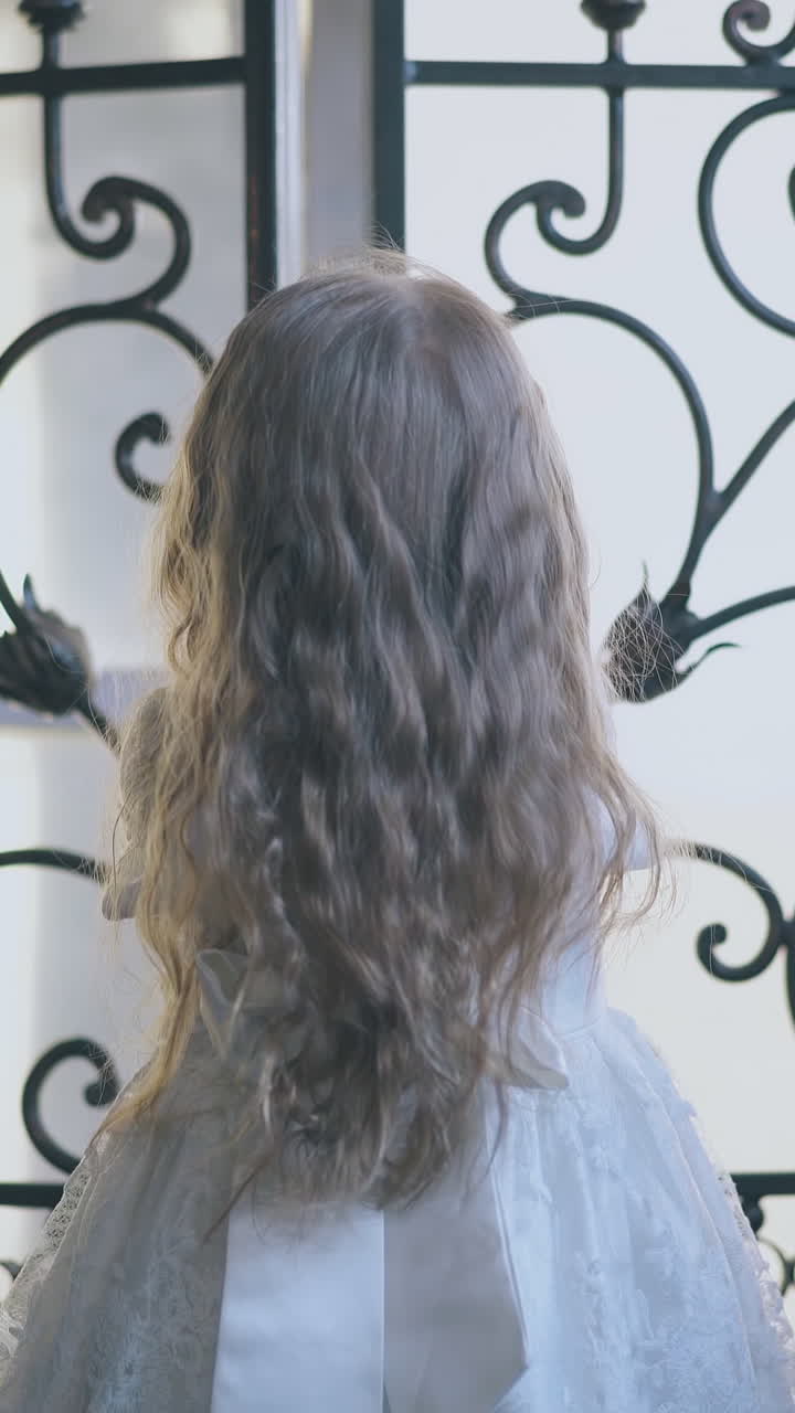 pretty blonde long haired girl in white holiday dress closes large forged lattice of room door at home close view