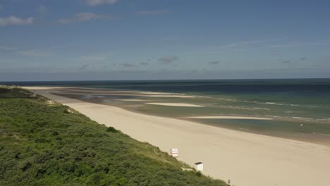 aerial shot flying over an empty beach towards a beautiful blue sea on a sunny day