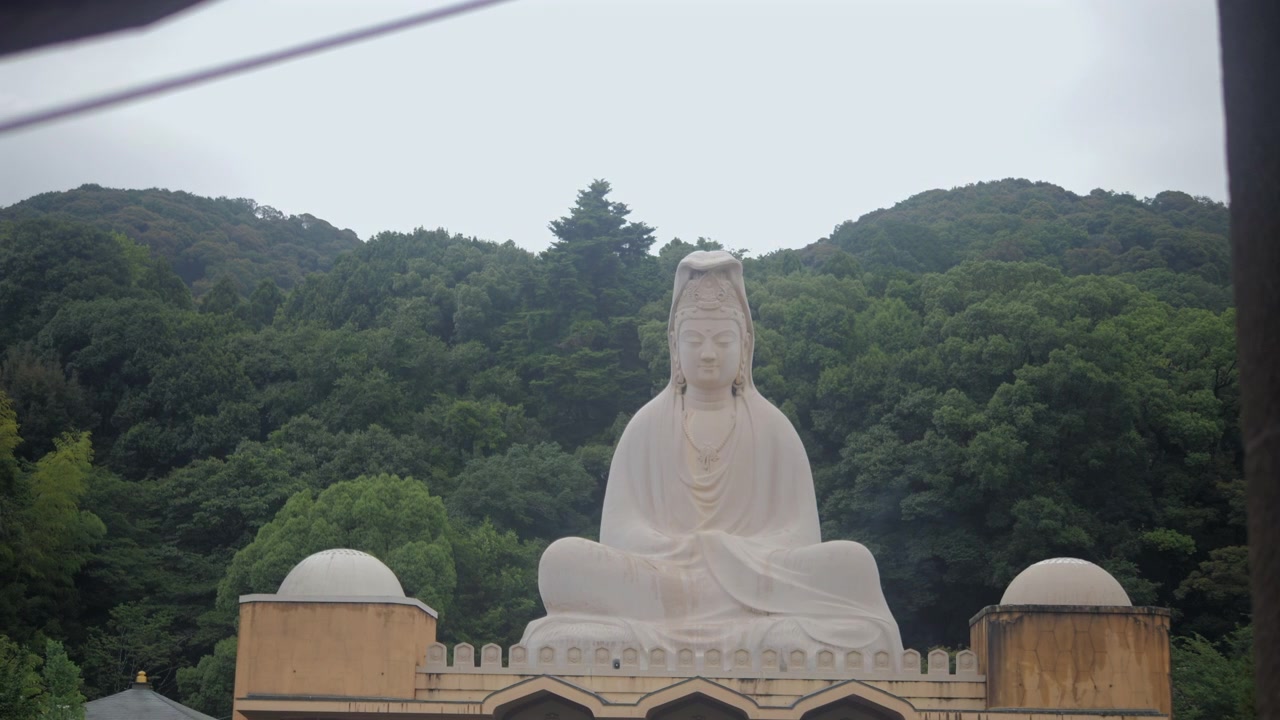 Stor hvid Buddha-statue i Kyoto med frodige grønne skovklædte bakker i baggrunden