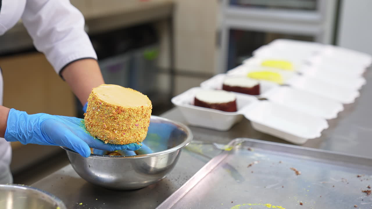 Food factory worker covers the cakes with yellow sprinkling. Close up. Ready-made desserts being put in separate boxes. Blurred backdrop.