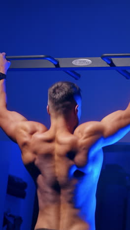 man training on horizontal bar in gym. back view portrait of young bodybuilder doing pull ups on the horizontal bar indoors. vertical video