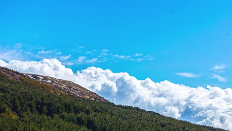 Time-lapse-of-thick-clouds-moving,-foaming-in-near-a-rocky-mountain-and-forest