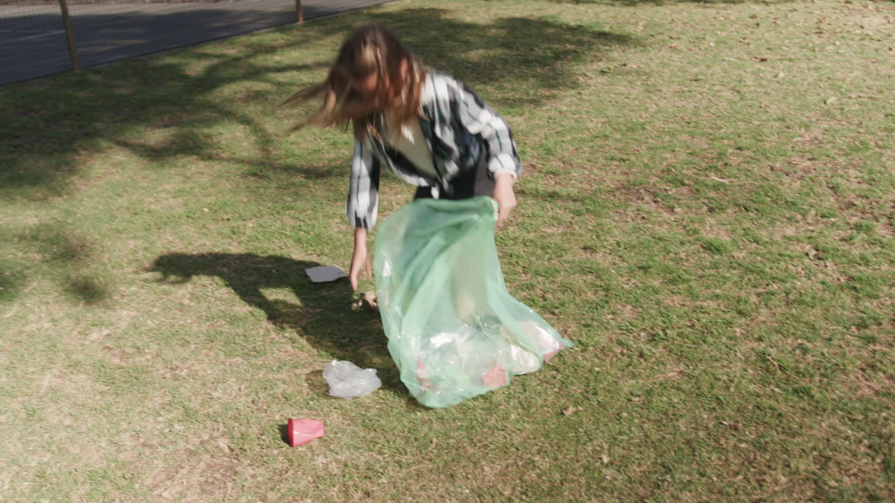 Girl cleaning park, picking up trash with green bag, promoting environmental care