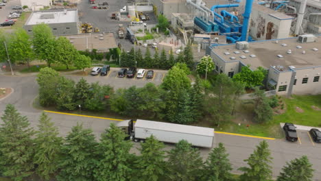 aerial tracking shot of loaded semi truck departing industrial factory