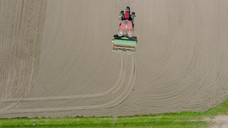 Aerial-view-of-plowed-field-with-tractor-sowing-seeds-of-wheat,-agricultural-theme,-farm-tractor-and-seeder-planting-crops-on-a-field-on-sunny-spring-day,-birdseye-drone-shot-moving-forward