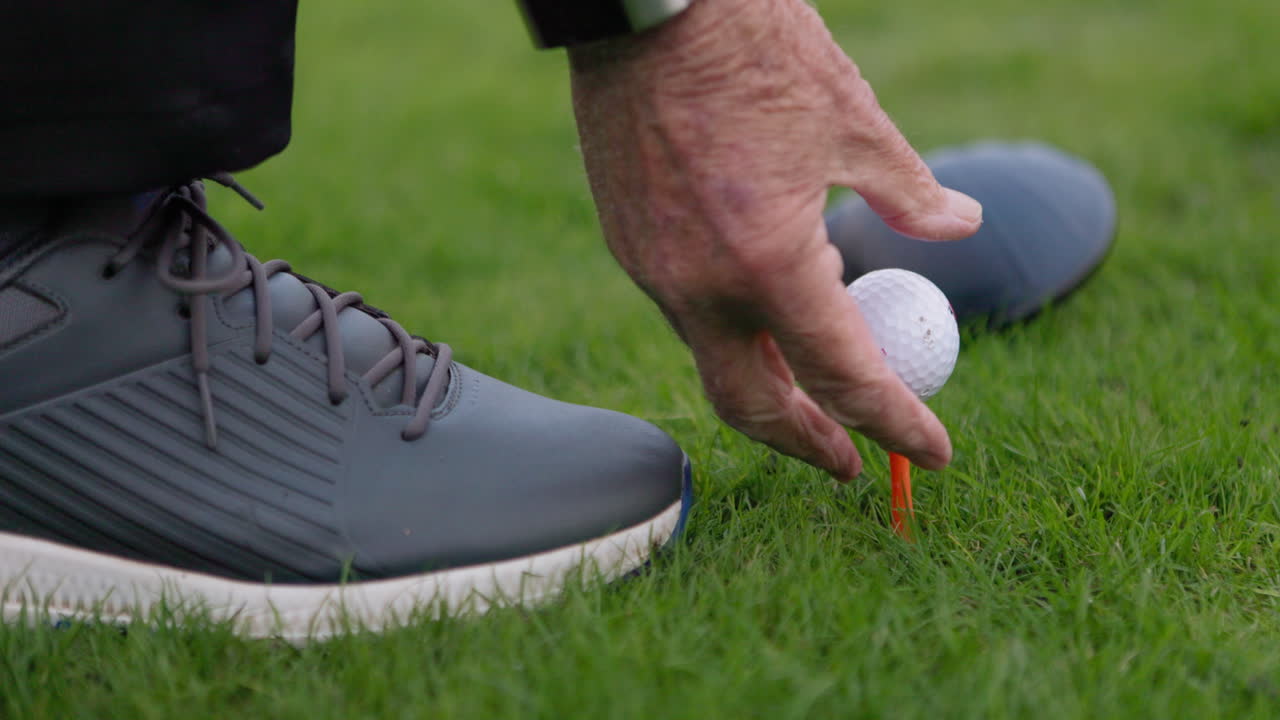 Golf ball on tee with golf club and shoe in background