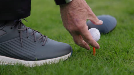 golf ball on tee with golf club and shoe in background