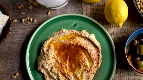 sliding to the left showing a flat lay plate of hummus with feta, olives, glass of ouzo, lemons, pine nuts on a rustic wood table