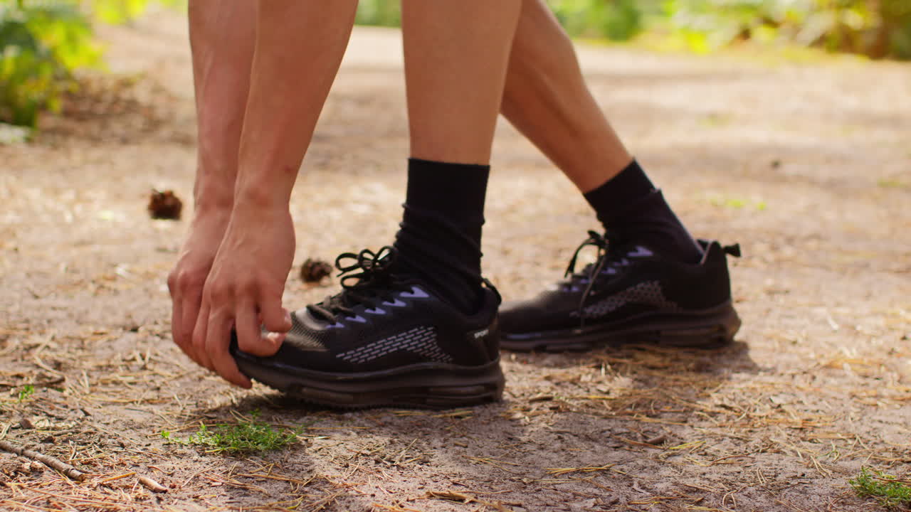 primer plano de un hombre con zapatos de entrenamiento calentándose estirando el pie antes de hacer ejercicio corriendo por la pista a través del bosque