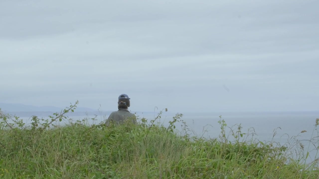 Mulher solitária em meio à vegetação, admirando o mar distante