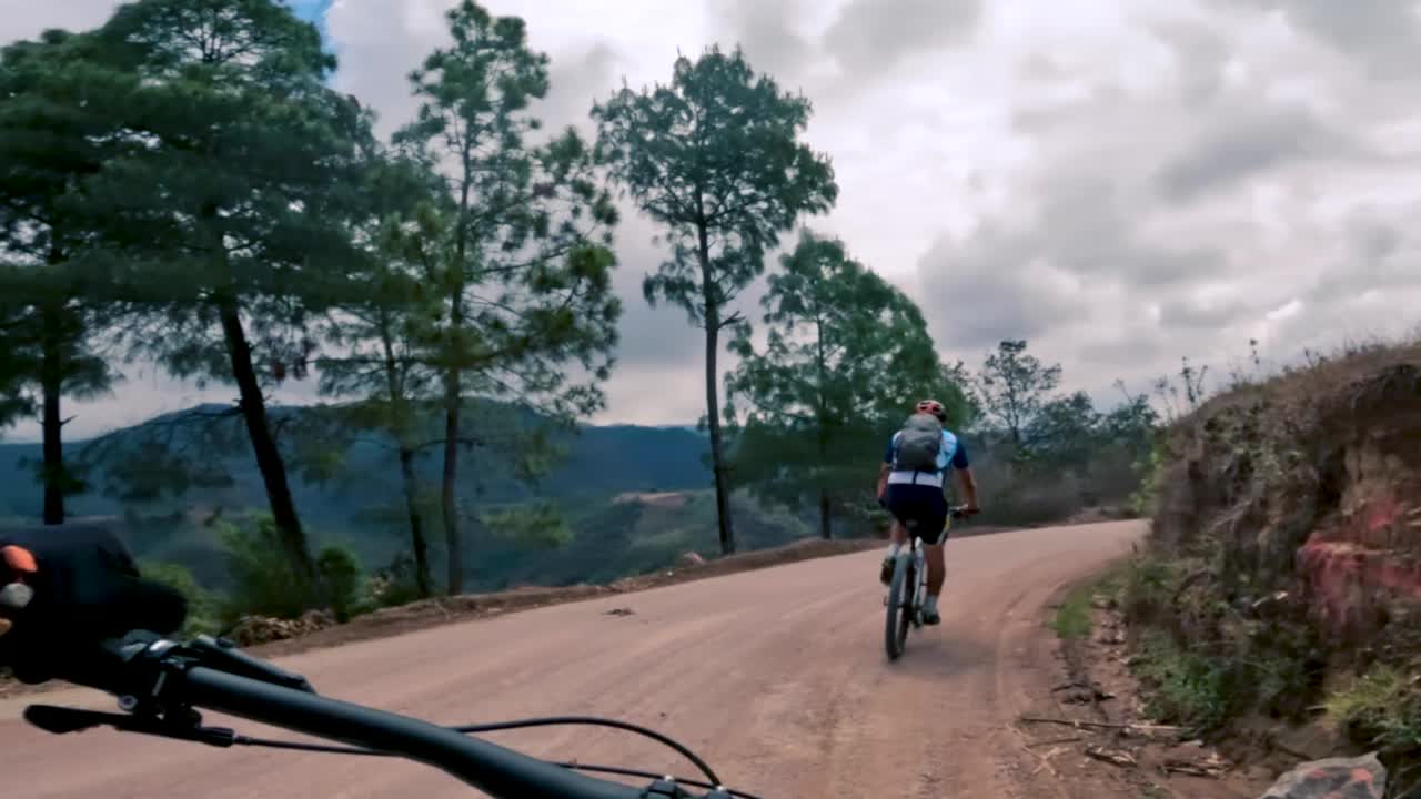 dos ciclistas andan en bicicleta por una carretera dentro de un bosque, una colina y un pueblo en guatemala, américa del norte
