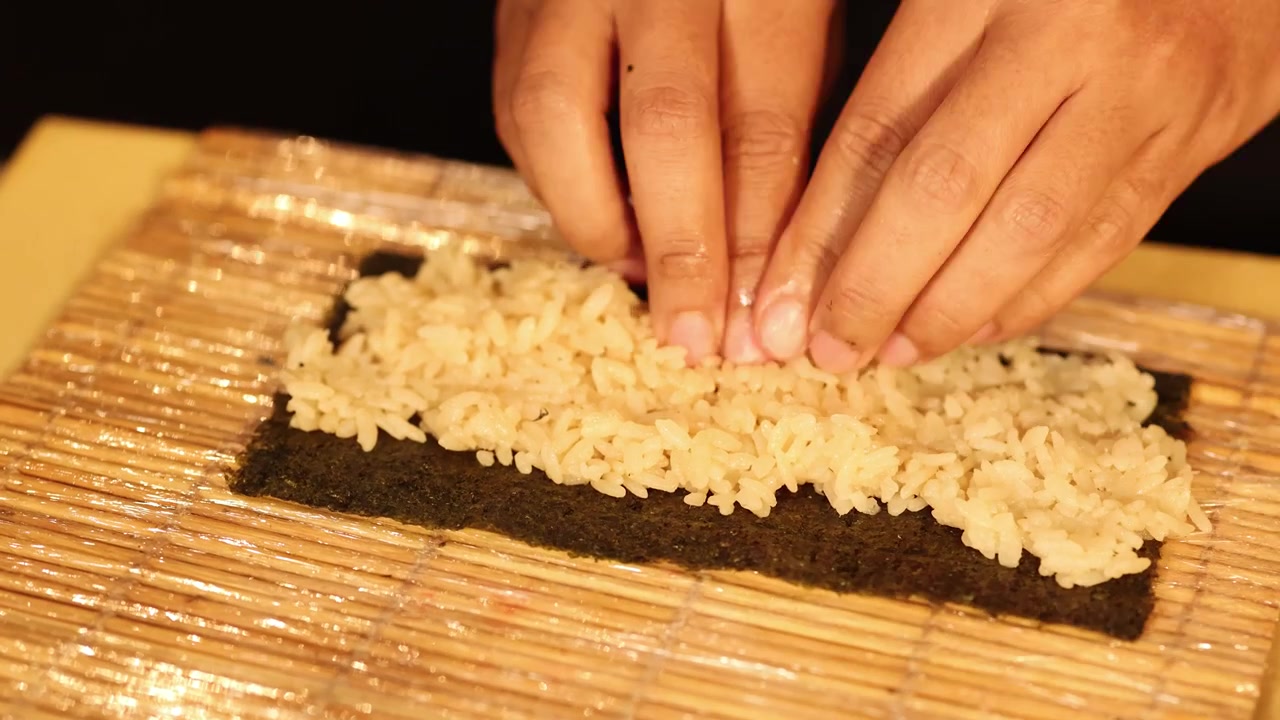 Primo piano di mani che stendono riso condito sull'alga nori usando una stuoia di bambù a Bangkok.