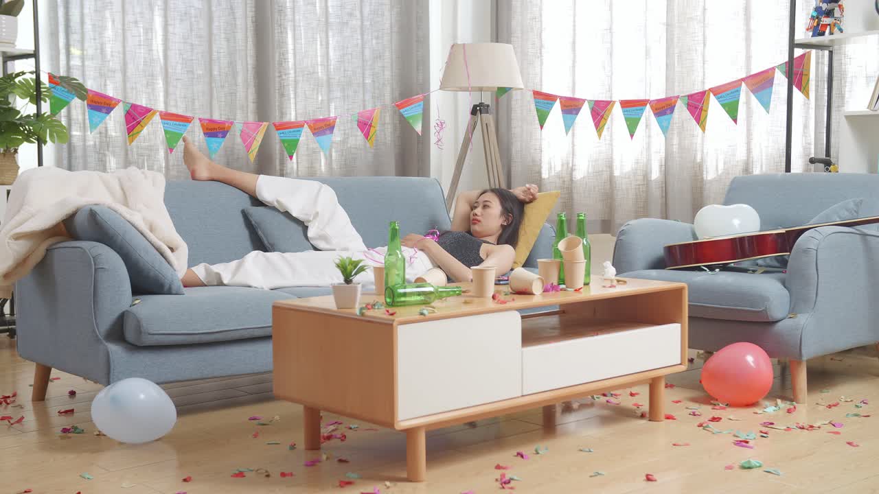 술에 취한 아시아 여성이 집에서 파티 방에서 소파에서 잠을 자고 깨어납니다.