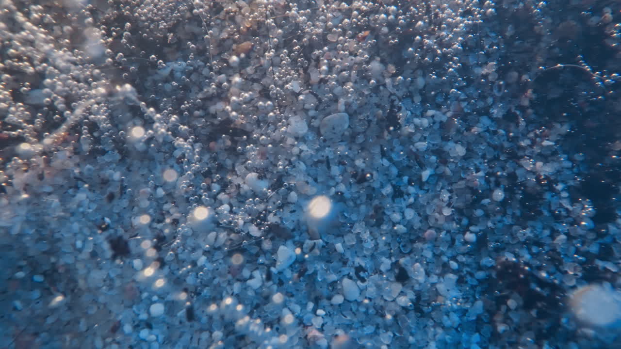 Dark dirt pieces fall down on sea bottom with small pebbles
