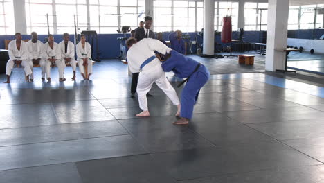 practicing judo, athletes sparring on mat while others watch in dojo