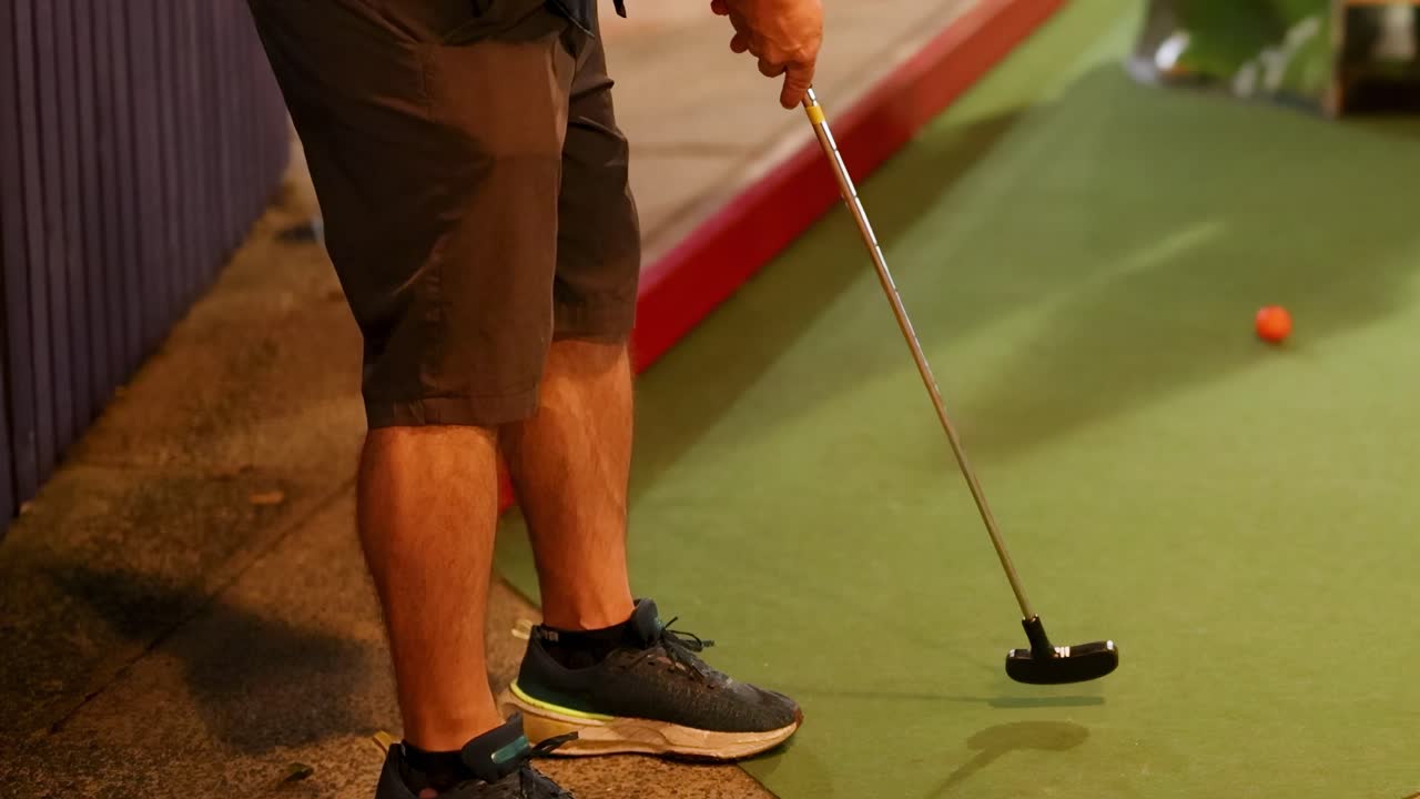 A person attempts a putt on an indoor mini golf course with colorful obstacles and ambient lighting