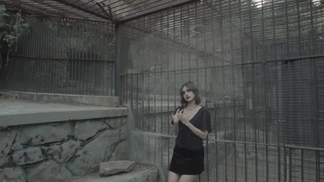 a beautiful young girl in a black dress trapped in a dark cage meditates and explores the surroundings