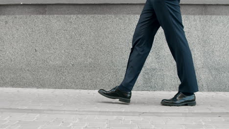 cropped image man walking in black shoes. closeup male feet going near building