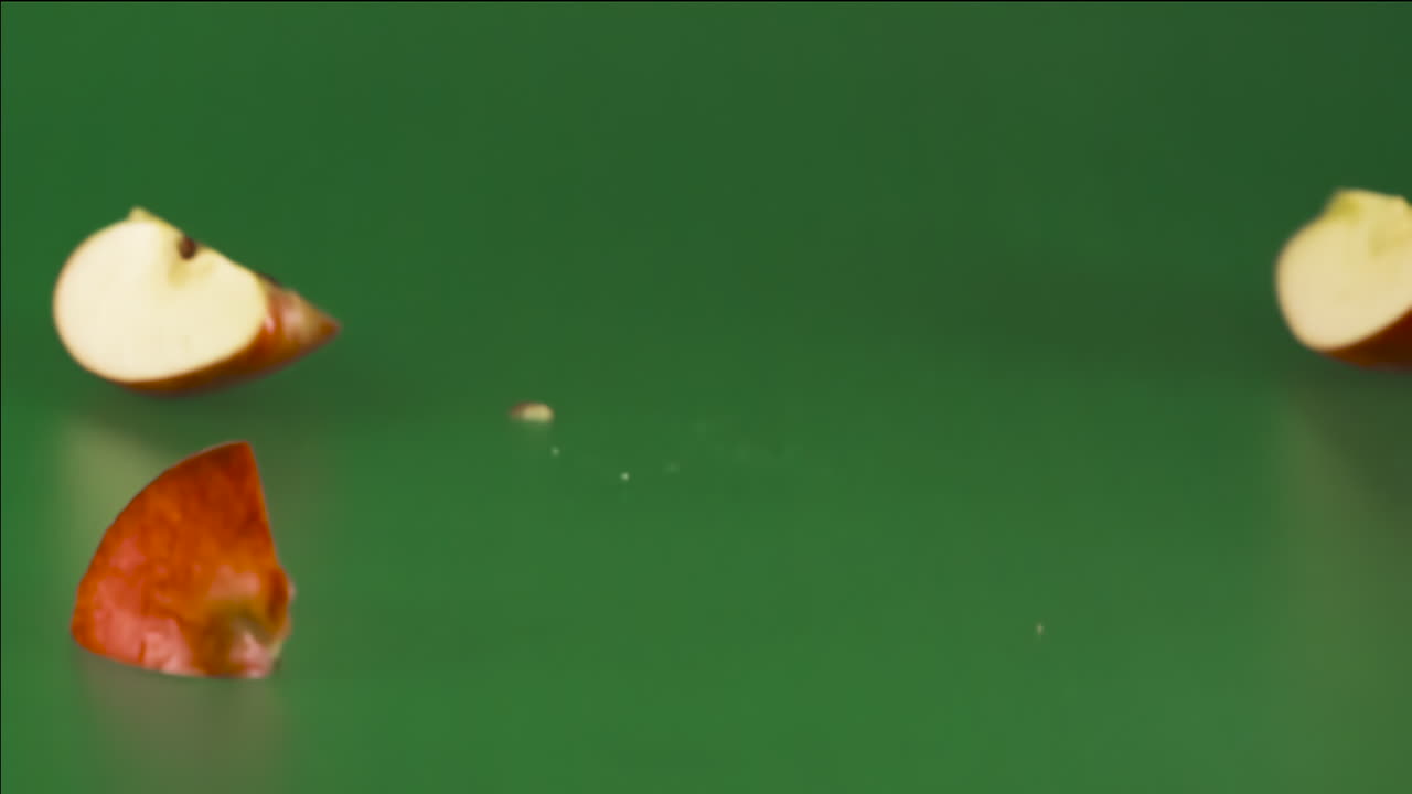 manzana roja cayendo y rompiéndose en muchos pedazos sobre un fondo verde