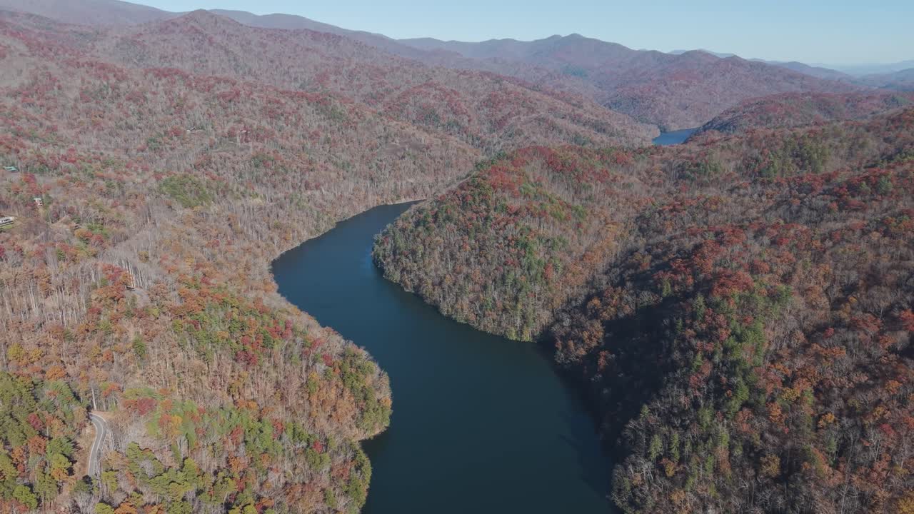 Great Smoky Dağları'nın canlı sonbahar renkleriyle çevrili Fontana Gölü'nün zümrüt yeşili sularının sinematik havadan çekimi.