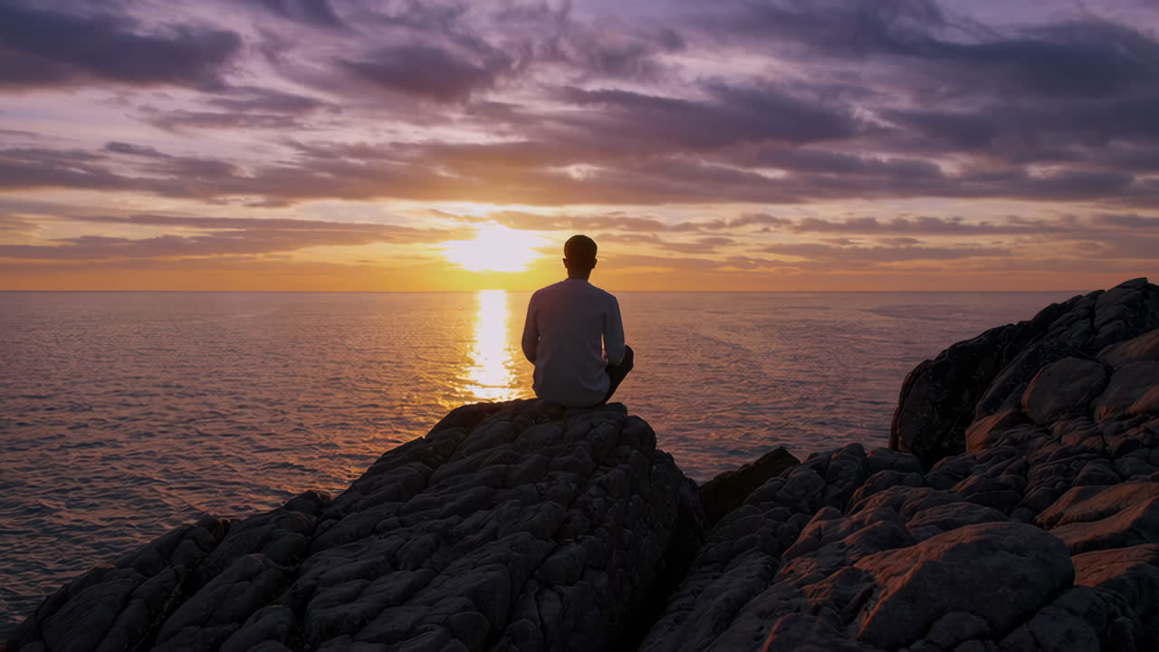 Man Sitting on Rocks at Sunset over the Ocean