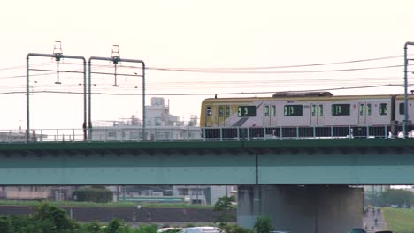 tren jr pasando por el puente en tamagawa con autos estacionados debajo en tokio, japón - toma panorámica