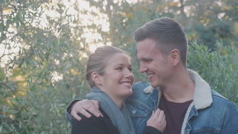 Portrait-Of-Loving-Young-Couple-Hugging-Outdoors-In-Fall-Or-Winter-Countryside-Against-Flaring-Sun