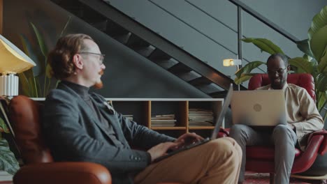 two businessmen using laptops and having discussion in comfortable office
