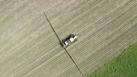 aerial top down, farm tractor spraying pesticide, herbicide and insecticide on agricultural farm field